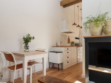 A small dining table with two chairs and a vase with greenery next to a kitchen with white cabinets and wooden countertops at The Apple Shed in Upexe near Silverton
