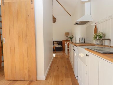 A narrow kitchen with wooden countertops and white cabinets next to a wooden sliding door at The Apple Shed in Upexe near Silverton