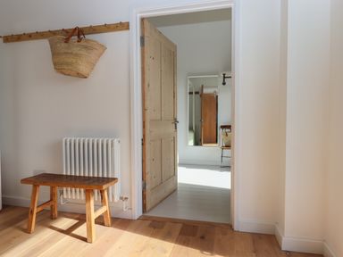 A wooden bench below a white radiator and a wooden door leading to a room with a mirror and a chair with a basket at The Apple Shed in Upexe near Silverton