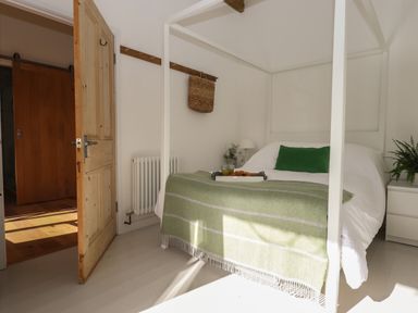 A bedroom with a white canopy bed with a green pillow and blanket a wooden door and a wicker basket on the wall at The Apple Shed in Upexe near Silverton