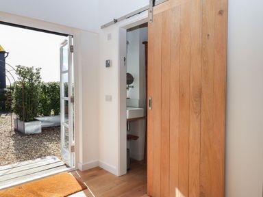 An entryway with a wooden sliding door partially open showing a bathroom sink and an open glass door leading to an outdoor gravel area with planters at The Apple Shed in Upexe near Silverton
