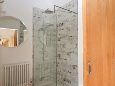 A bathroom with a walk in shower and a round mirror on the wall at The Apple Shed in Upexe near Silverton