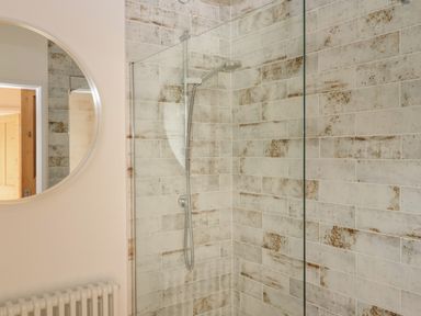 A bathroom with a walk-in shower with tiled walls a round mirror and a radiator at The Apple Shed in Upexe near Silverton