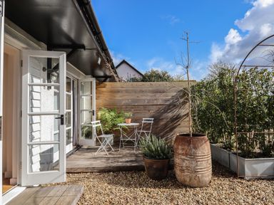 An outdoor patio with white open doors a small white table and chairs wooden fence and potted plants at The Apple Shed in Upexe near Silverton