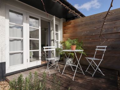 An outdoor patio with a white round table and two white chairs next to wooden fence and glass doors at The Apple Shed in Upexe near Silverton