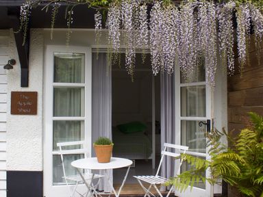 An outdoor seating area with a white table and two chairs under hanging flowers at The Apple Shed in Upexe near Silverton