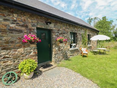 A stone house with a green door two hanging flower baskets and outdoor seating with an umbrella at Bohan Bo in Tinteskin near Kilmuckridge County Wexford