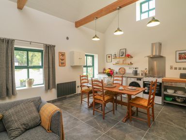 A kitchen with wooden dining table and chairs a couch by the window and cooking appliances at Bohan Bo in Tinteskin near Kilmuckridge County Wexford