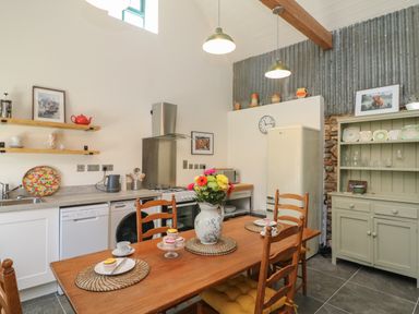 A kitchen with wooden dining table and chairs a vase with flowers a refrigerator and shelves with cups and plates at Bohan Bo in Tinteskin near Kilmuckridge County Wexford