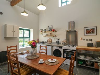 A kitchen with wooden dining table and chairs with cushions a vase of flowers a stove washing machine and microwave at Bohan Bo Tinteskin near Kilmuckridge County Wexford