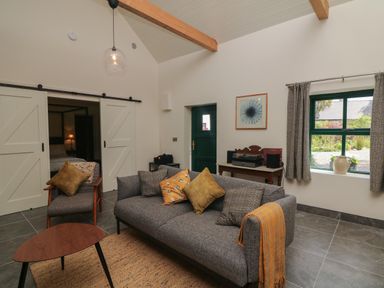 A living room with a gray sofa and armchair with cushions a wooden coffee table and a side table with a record player and speakers at Bohan Bo in Tinteskin near Kilmuckridge County Wexford