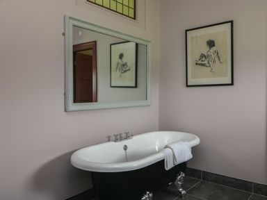 A bathroom with a clawfoot bathtub with a towel over the side a wall mirror and a framed drawing at Bohan Bo in Tinteskin near Kilmuckridge County Wexford
