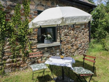 An outdoor table with two chairs and an umbrella next to a stone wall with a window and plants at Bohan Bo in Tinteskin near Kilmuckridge County Wexford