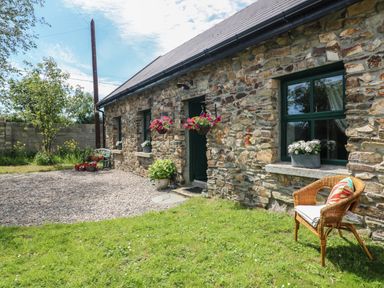 Exterior of a stone building with green framed windows a wicker chair with cushion hanging flower baskets and potted plants at Bohan Bo in Tinteskin near Kilmuckridge County Wexford