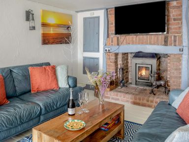 A living room with two leather sofas a wooden coffee table and a brick fireplace with a television above at The Cubby Hole in Sennen Cove