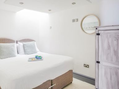 A bedroom with a double bed with pillows and a tray on top a round mirror and a wooden cabinet on the wall at The Cubby Hole in Sennen Cove