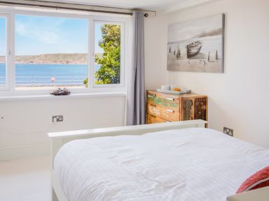 A bedroom with a white bed a distressed wooden dresser and a window showing a sea view at The Cubby Hole in Sennen Cove