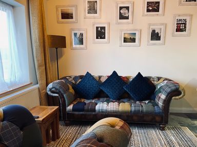 A living room with a patchwork sofa with three blue cushions a wooden side table and framed pictures on the wall at Harvest Moon Cottage in Much Cowarne
