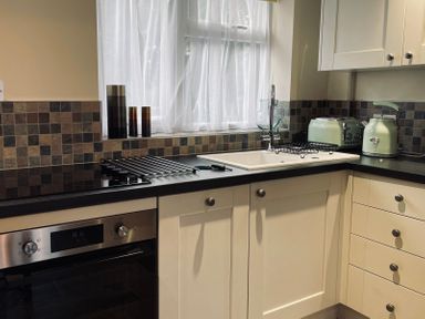 A kitchen with white cabinets black countertop a stove oven sink toaster kettle and three decorative containers on the windowsill at Harvest Moon Cottage in Much Cowarne