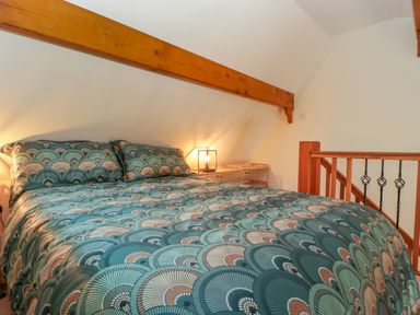 A bedroom with a patterned bedspread wooden beams and a bedside lamp at Harvest Moon Cottage in Much Cowarne