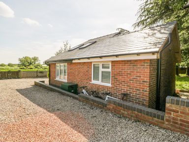 Exterior view of a brick house with a tiled roof two white windows bicycles leaning against a low brick wall and gravel ground at Harvest Moon Cottage in Much Cowarne