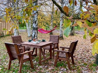 A wooden table and four chairs under trees with autumn leaves and a red hammock in the background at Harvest Moon Cottage in Much Cowarne