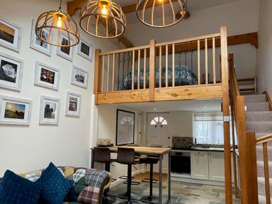 A kitchen and living area with bar stools and a loft bed above at Harvest Moon Cottage in Much Cowarne