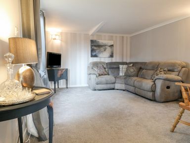 A living room with a gray sectional sofa and a small TV on a stand at The Lodge at Wildersley Farm in Belper