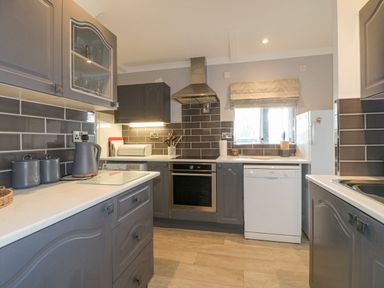 A kitchen with grey cabinets white countertops a stove dishwasher and window at The Lodge at Wildersley Farm in Belper