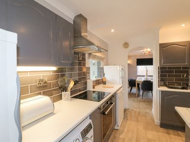 A kitchen with dark cabinets stove and kitchen utensils leading to a dining room at The Lodge at Wildersley Farm in Belper