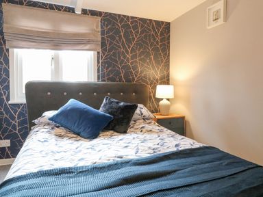 A bedroom with a bed with blue and grey pillows and a bedside table with a lamp at The Lodge at Wildersley Farm in Belper