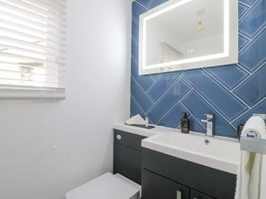 A bathroom with a sink cabinet a mirror with light blue tiles on the wall and a window with blinds at The Lodge at Wildersley Farm in Belper