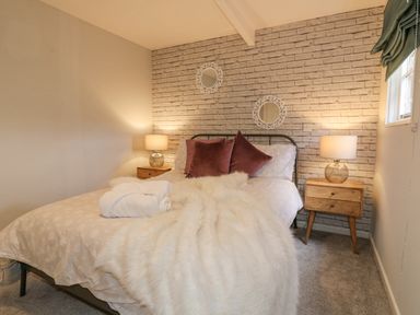 A bedroom with a bed flanked by two wooden nightstands and lamps at The Lodge at Wildersley Farm in Belper
