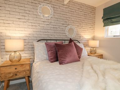 A bedroom with a bed between two wooden nightstands with lamps and a window with a green roman shade at The Lodge at Wildersley Farm in Belper