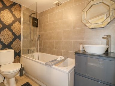 A bathroom with a toilet bathtub with shower and a sink with a mirror above at The Lodge at Wildersley Farm in Belper