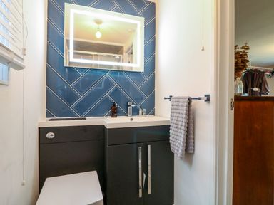 A bathroom with a sink cabinet and illuminated mirror above blue tiled wall at The Lodge at Wildersley Farm in Belper