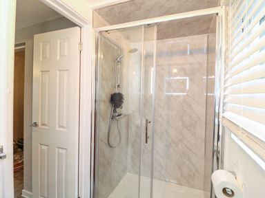 A bathroom with a glass shower enclosure a showerhead and a window with blinds near a door at The Lodge at Wildersley Farm in Belper