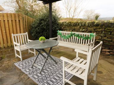 An outdoor seating area with a round table a potted plant two wooden chairs a bench with green garland and a patterned rug at The Lodge at Wildersley Farm in Belper