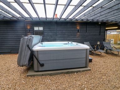 An outdoor covered area with a hot tub and two lounge chairs at The Lodge at Wildersley Farm in Belper