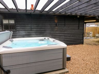An outdoor hot tub under a pergola with a black wooden wall and a seating area at The Lodge at Wildersley Farm in Belper