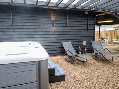 An outdoor area with a hot tub two lounge chairs a small table and wooden fencing at The Lodge at Wildersley Farm in Belper