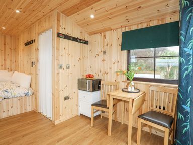 A wooden interior room with a small table and two chairs next to a window and a microwave on a white cabinet at Tal Sarn Shepherd Hut in Dwyran near Niwbwrch Newborough
