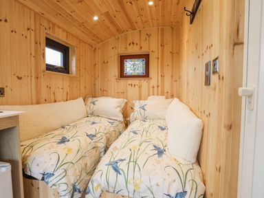 A small bedroom with two single beds with patterned bedding in a wooden room at Tal Sarn Shepherd Hut in Dwyran near Niwbwrch Newborough