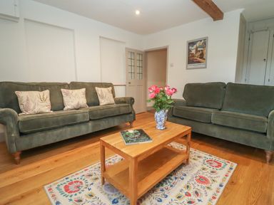 A living room with two green sofas a wooden coffee table with flowers and a book on a patterned rug at Blossom Cottage in Chipping Campden