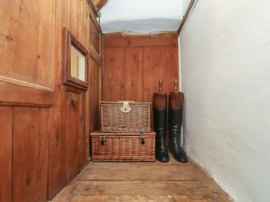 A corner with wooden paneling containing two woven baskets and a pair of black riding boots with wooden boot trees