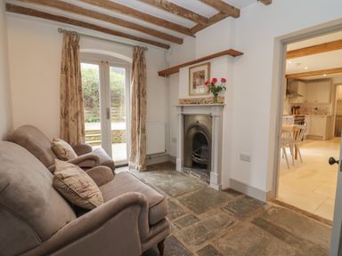A sitting room with two armchairs a fireplace and a door leading outside at Blossom Cottage in Chipping Campden