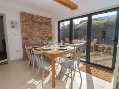 A dining area with a wooden table and six chairs next to a glass sliding door showing an outdoor patio at Blossom Cottage in Chipping Campden