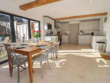 A kitchen with a wooden dining table set for six and white cabinets at Blossom Cottage in Chipping Campden