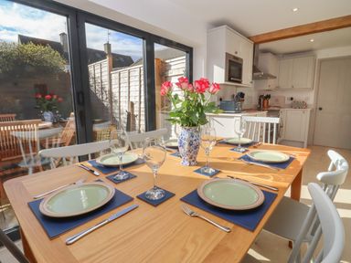 A dining table set with plates, wine glasses, and cutlery in a kitchen with glass doors showing an outdoor patio at Blossom Cottage in Chipping Campden
