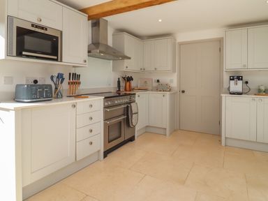 A kitchen with white cabinets a stainless steel oven a microwave toaster and coffee machine at Blossom Cottage in Chipping Campden